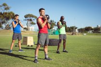 Groupe diversifié d'hommes musclés faisant de l'exercice avec des cloches de bouilloire à l'extérieur. mode de vie actif sain, entrainement croisé pour le concept de fitness. — Photo de stock