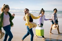 Щаслива група різноманітних друзів розважається, ходить вздовж пляжу тримаючи руки і сміючись. свято, свобода і дозвілля на відкритому повітрі . — стокове фото
