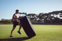 Shirtlos fit kaukasischer Mann, der im Freien trainiert und schwere Reifen anhebt. gesunder aktiver Lebensstil, Crosstraining für Fitness. — Stockfoto