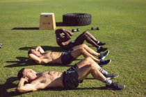 Grupo diverso de homens musculosos fazendo crunches exercitando ao ar livre. estilo de vida ativo saudável, treinamento cruzado para conceito de aptidão. — Fotografia de Stock
