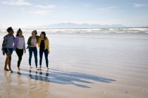 Счастливая группа разнообразных подруг, веселящихся, гуляющих по пляжу, держась за руки и смеющихся. отдых, свобода и досуг на открытом воздухе. — стоковое фото