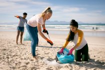 Diverse Frauen laufen am Strand entlang und sammeln Müll auf. Freiwillige Umweltschützer, Säuberung des Strandes. — Stockfoto
