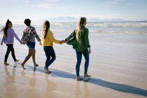 Grupo feliz de amigas divertidas se divertindo, andando ao longo da praia de mãos dadas e rindo. férias, liberdade e lazer ao ar livre. — Fotografia de Stock
