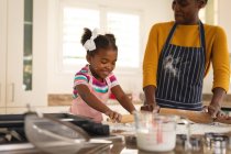 Sonriente madre afroamericana y su hija horneando en la cocina rodando masa juntos. familia pasar tiempo juntos en casa. - foto de stock