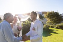 Felici sposi caucasici che si sposano stringendo la mano all'officiante del matrimonio. matrimonio estivo, matrimonio, amore e concetto di celebrazione. — Foto stock