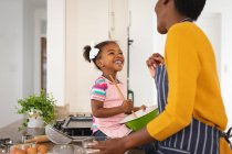 Lächelnde afrikanisch-amerikanische Mutter und Tochter beim gemeinsamen Backen in der Küche. Familie verbringt Zeit zu Hause. — Stockfoto