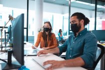 Dois empresários diversos usando máscara facial usando computador. trabalho em um escritório moderno durante covid 19 coronavirus pandemia. — Fotografia de Stock