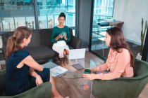 Eine Gruppe unterschiedlicher Geschäftsfrauen diskutiert zusammen am Glastisch und bedient sich eines Laptops. Arbeit in einem modernen Büro. — Stockfoto