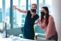 Due donne d'affari caucasiche che indossano la maschera e discutono. lavoro in un ufficio moderno durante covid 19 coronavirus pandemia. — Foto stock