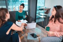 Grupo de diversas mulheres de negócios discutindo juntos sentado à mesa de vidro e usando laptop. trabalho em um escritório moderno. — Fotografia de Stock
