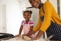 Smiling african american mother and daughter baking in kitchen rolling dough together. family spending time together at home. — Stock Photo