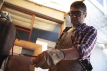 Caucasian male knife maker wearing apron and glasses, making knife in workshop. independent small business craftsman at work. — Stock Photo