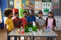 Grupo de estudiantes diversos que usan máscaras faciales que ponen artículos plásticos reciclables en bandeja en la escuela. educación volver a la escuela seguridad sanitaria durante la pandemia de coronavirus covid19. - foto de stock