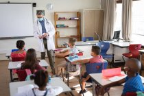 Kaukasischer Arzt mit Mundschutz, der Schülern in der Schule zeigt, wie man Händedesinfektionsmittel anwendet. Gesundheitsschutz und Sicherheit in der Schule während des Covid-19-Pandemiekonzepts — Stockfoto