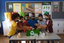 Gruppo di studenti diversi che indossano maschere per il viso mettendo oggetti di plastica riciclabili nel vassoio a scuola. educazione alla sicurezza sanitaria scolastica durante la pandemia di coronavirus covid19. — Foto stock