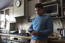 Konzentrierter Kaukasier, der in der Küche steht, Smartphone benutzt und entspannt. Freizeit zu Hause verbringen. — Stockfoto