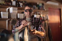 Kaukasischer Messermacher mit Schürze und Brille, der Messer in der Werkstatt herstellt. unabhängiger Kleinunternehmer bei der Arbeit. — Stockfoto