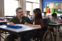 Insegnante maschio caucasico che insegna disabile ragazza caucasica seduta sulla sedia a rotelle in classe a scuola. concetto di scuola e istruzione — Foto stock