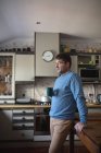 Фокусований білий чоловік стоїть на кухні п'є каву і використовує смартфон. вільний час вдома . — стокове фото