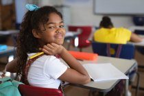 Porträt eines afrikanisch-amerikanischen Mädchens, das in der Schulklasse auf ihrem Schreibtisch sitzt. Schul- und Bildungskonzept — Stockfoto