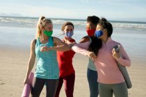 Группа разнообразных подруг в маске для лица практикует йогу, стоя и на пляже. здоровый активный образ жизни, фитнес на открытом воздухе и благополучие во время ковида 19 пандемии. — стоковое фото