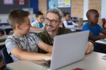 Insegnante maschio caucasico che insegna a un ragazzo caucasico come usare il portatile in classe a scuola. concetto di scuola e istruzione — Foto stock