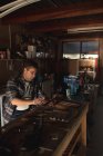 Kaukasischer Messermacher sitzt am Schreibtisch und benutzt Tabletten in der Werkstatt. unabhängiger Kleinunternehmer bei der Arbeit. — Stockfoto