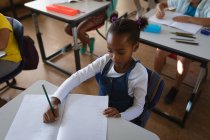 Afroamerikanerin lernt, während sie in der Schulklasse auf ihrem Schreibtisch sitzt. Schul- und Bildungskonzept — Stockfoto