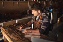 Coltellinaio caucasico seduto alla scrivania, che prende appunti in officina. artigiano indipendente delle piccole imprese al lavoro. — Foto stock