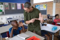 Caucasian male teacher and african american boy talking in hand sign language at school. school and education concept — Stock Photo