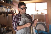 Fabricante de cuchillo masculino caucásico con delantal y gafas, haciendo cuchillo en el taller. artesano independiente de la pequeña empresa en el trabajo. - foto de stock