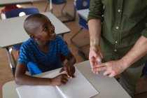 In der Mitte ein männlicher Lehrer, der in der Schule mit einem afrikanisch-amerikanischen Jungen in Gebärdensprache spricht. Schul- und Bildungskonzept — Stockfoto