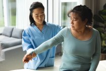 Азиатская женщина-физиотерапевт лечит пожилую пациентку у себя дома. медицинское и физиотерапевтическое лечение. — стоковое фото