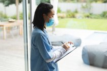 Asian female physiotherapist wearing face mask and writing on clipboard at home before treatment. healthcare and medical physiotherapy treatment. — Stock Photo