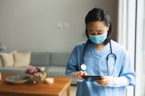 Asian female physiotherapist wearing face mask and using tablet at home before treatment. healthcare and medical physiotherapy treatment. — Stock Photo