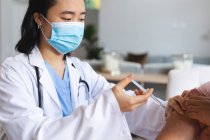 Asiatische Ärztin mit Gesichtsmaske und geimpfte Patientin zu Hause. Gesundheitswesen und medizinische physiotherapeutische Behandlung. — Stockfoto