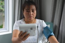 Asian woman sitting on couch and measuring pressure at home. healthcare and medical physiotherapy treatment. — Stock Photo