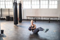 Mujer caucásica fuerte haciendo ejercicio en el gimnasio, haciendo abdominales usando pelota. entrenamiento cruzado de fuerza y fitness para boxeo. - foto de stock
