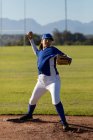 Mixed race female baseball pitcher on sunny baseball field throwing ball during game. female baseball team, sports training and game tactics. — Stock Photo
