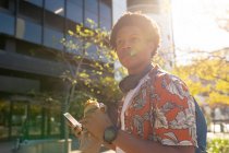 Африканский американец в городе ест и пользуется смартфоном. цифровая реклама на ходу, на улице и по городу. — стоковое фото
