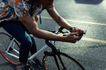 Африканский американец в городе сидит на велосипеде и пользуется смартфоном. цифровая реклама на ходу, на улице и по городу. — стоковое фото
