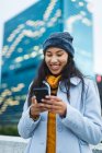 Asiatin mit Smartphone und lächelnd auf der Straße. Unabhängige junge Frau in der Stadt unterwegs. — Stockfoto