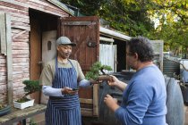 Zwei unterschiedliche Männer nutzen das kontaktlose Bezahlen im Gartencenter. Spezialisten in der Bonsai-Gärtnerei, selbstständiger Gartenbaubetrieb. — Stockfoto