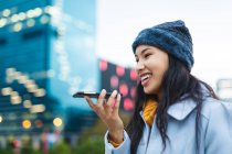 Азійка користується смартфоном і посміхається на вулиці. Незалежна молода жінка у місті.. — стокове фото