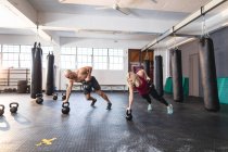 Белый мужчина и женщина тренируются в спортзале, отжимаются с помощью гирь. силовые и фитнес-кросс тренировки для бокса. — стоковое фото