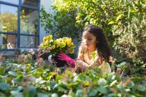 Sonriente chica de raza mixta plantando flores en el patio trasero. estilo de vida doméstico y pasar tiempo de calidad en casa. - foto de stock