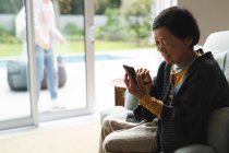 Felice anziana donna asiatica a casa utilizzando smartphone. stile di vita senior, tecnologia, trascorrere del tempo a casa. — Foto stock