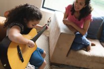 Mutter und Tochter sitzen auf dem Sofa und spielen Gitarre. Lebensstil und hochwertige Zeit zu Hause verbringen. — Stockfoto