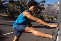Un uomo afroamericano in forma che si allunga in citta 'per strada. fitness e stile di vita urbano attivo all'aperto. — Foto stock