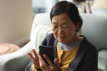 Feliz mujer asiática senior en casa usando smartphone. estilo de vida senior, tecnología, pasar tiempo en casa. - foto de stock